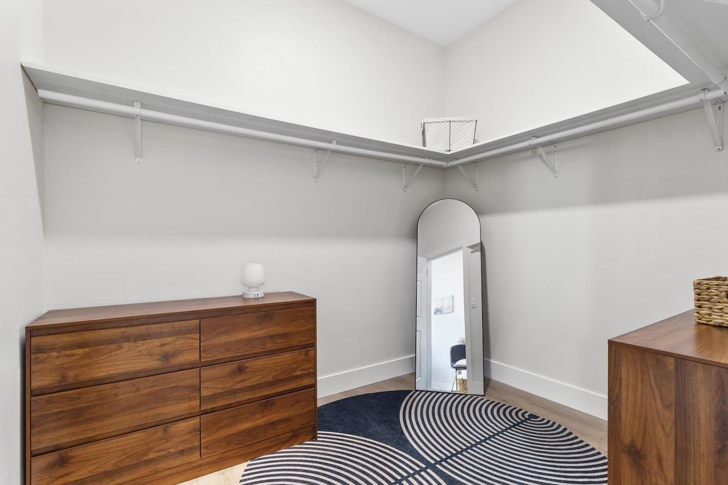 A corner room with a wooden dresser, a mirror, a patterned rug, and a ceiling with a skylight.