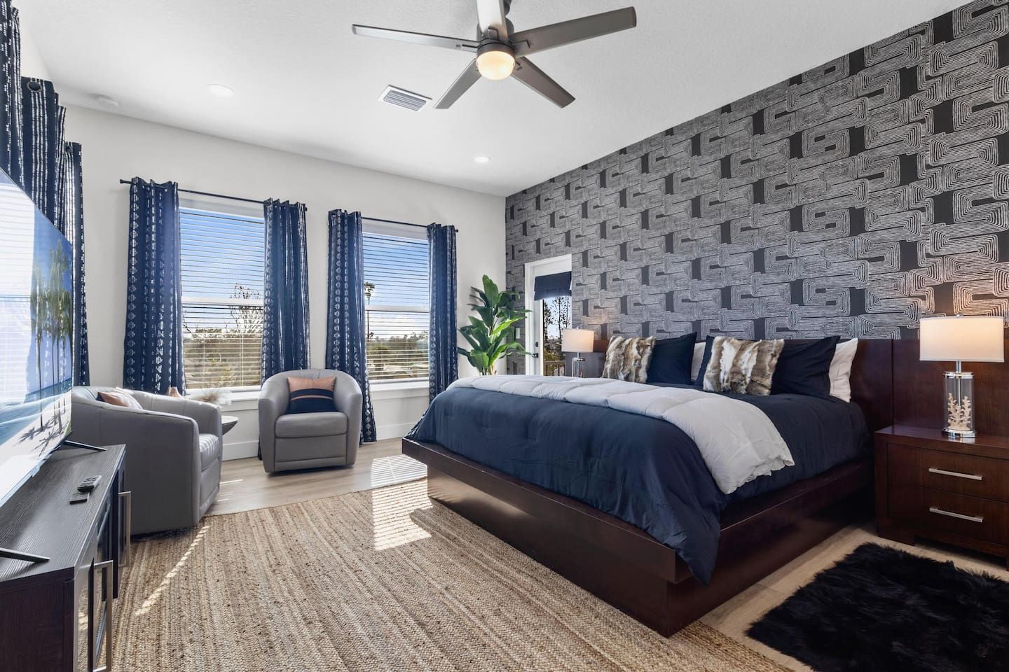 A bedroom with a large bed, a desk, a chair, and a ceiling fan.