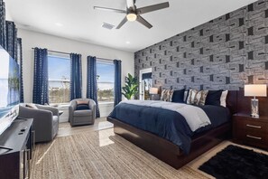 A bedroom with a large bed, a desk, a chair, and a ceiling fan.