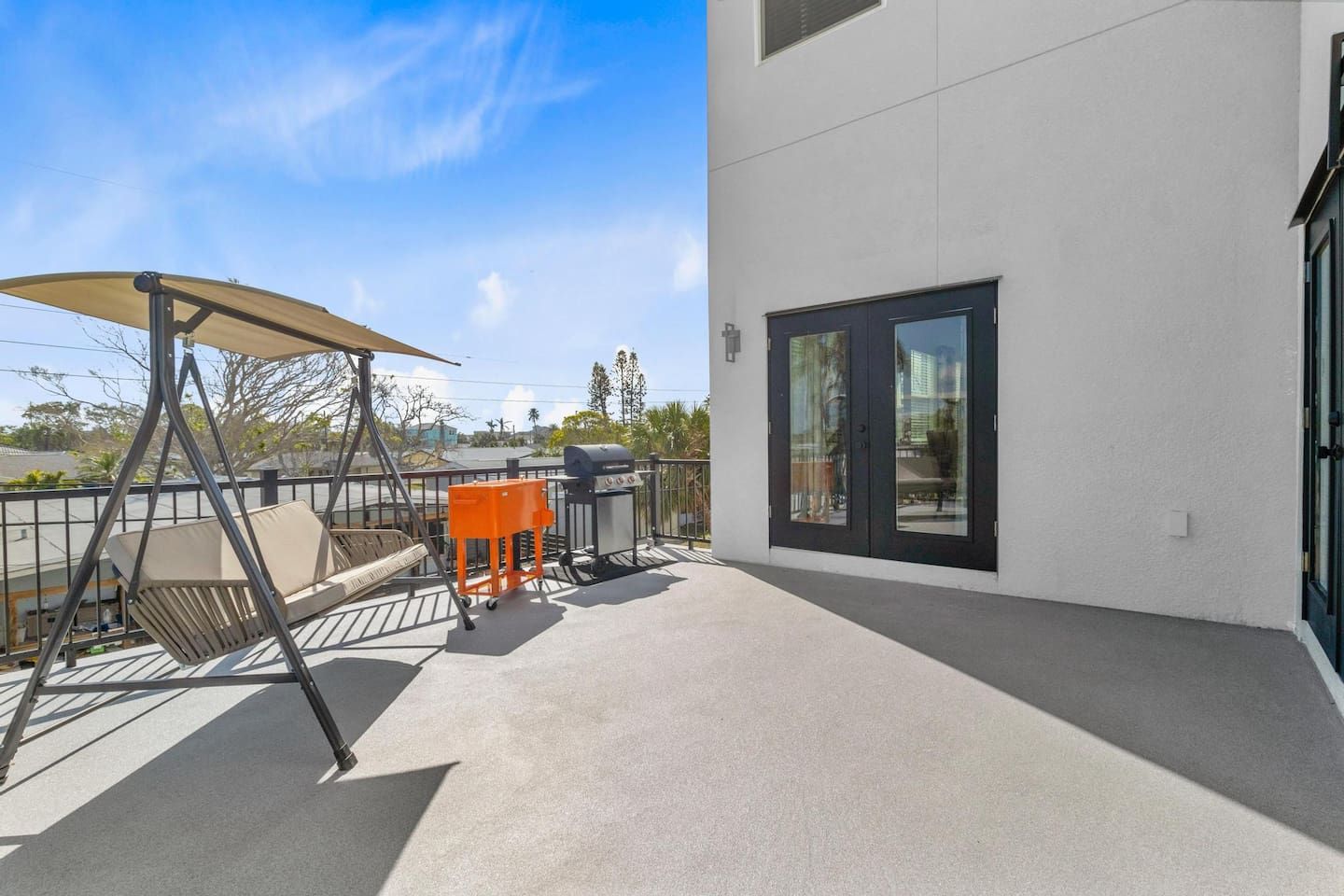 A balcony with a swing chair, a grill, and a table.