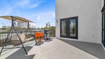 A balcony with a swing chair, a grill, and a table.