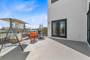A balcony with a swing chair, a grill, and a table.