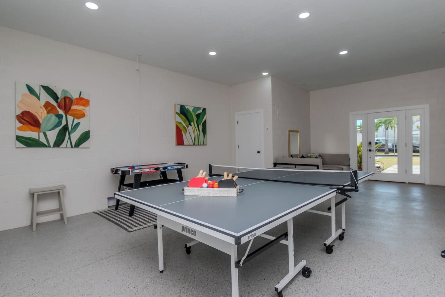 Una mesa de ping pong con una raqueta y pelotas de tenis de mesa, una mesa de fútbol de mesa y dos cuadros en la pared.