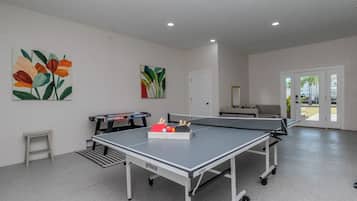 Una mesa de ping pong con una raqueta y pelotas de tenis de mesa, una mesa de fútbol de mesa y dos cuadros en la pared.