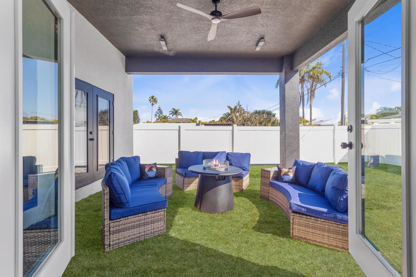 An outdoor patio with wicker furniture and a round table, featuring a clear view of the sky and distant trees.