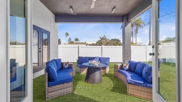 An outdoor patio with wicker furniture and a round table, featuring a clear view of the sky and distant trees.