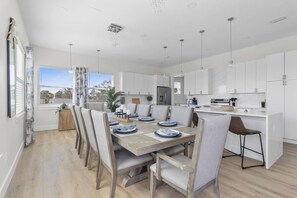 A modern kitchen with white cabinets, a dining area with a wooden table and chairs, and a view of the outside.