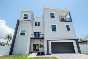 A modern two-story residential building with a garage, a balcony, and a small front yard.