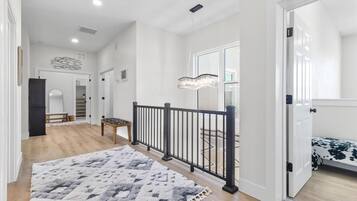 A spacious hallway with a wooden floor, a black railing, and a patterned rug.