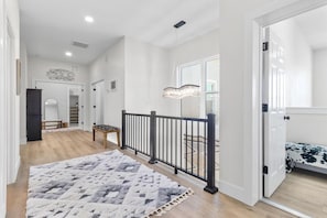 A spacious hallway with a wooden floor, a black railing, and a patterned rug.