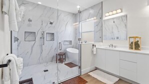 A modern bathroom with a glass-enclosed shower, a vanity with a mirror, and a small wooden stool. - 3 Blocks to Redington Beach | Sleeps 10, 6BR (Redington Beach)