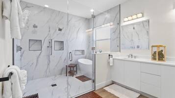 A modern bathroom with a glass-enclosed shower, a vanity with a mirror, and a small wooden stool.