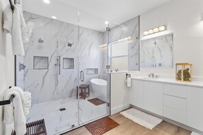 A modern bathroom with a glass-enclosed shower, a vanity with a mirror, and a small wooden stool.