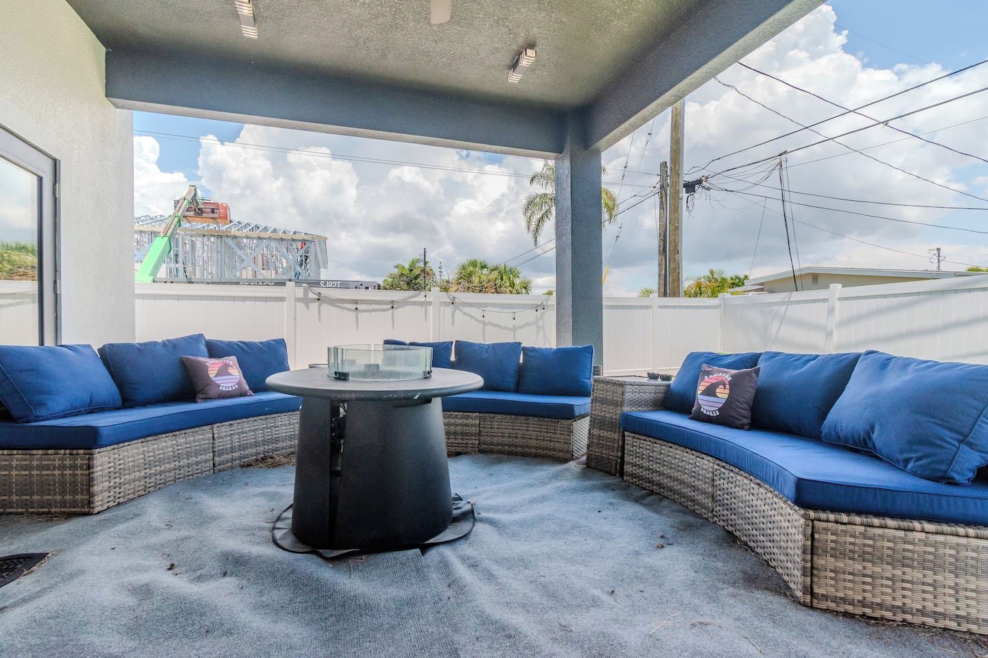 Un espace extérieur aménagé avec des meubles de jardin, comprenant des canapés bleus avec coussins et une table centrale, et offrant une vue sur un quartier résidentiel.
