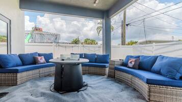 Un espace extérieur aménagé avec des meubles de jardin, comprenant des canapés bleus avec coussins et une table centrale, et offrant une vue sur un quartier résidentiel.