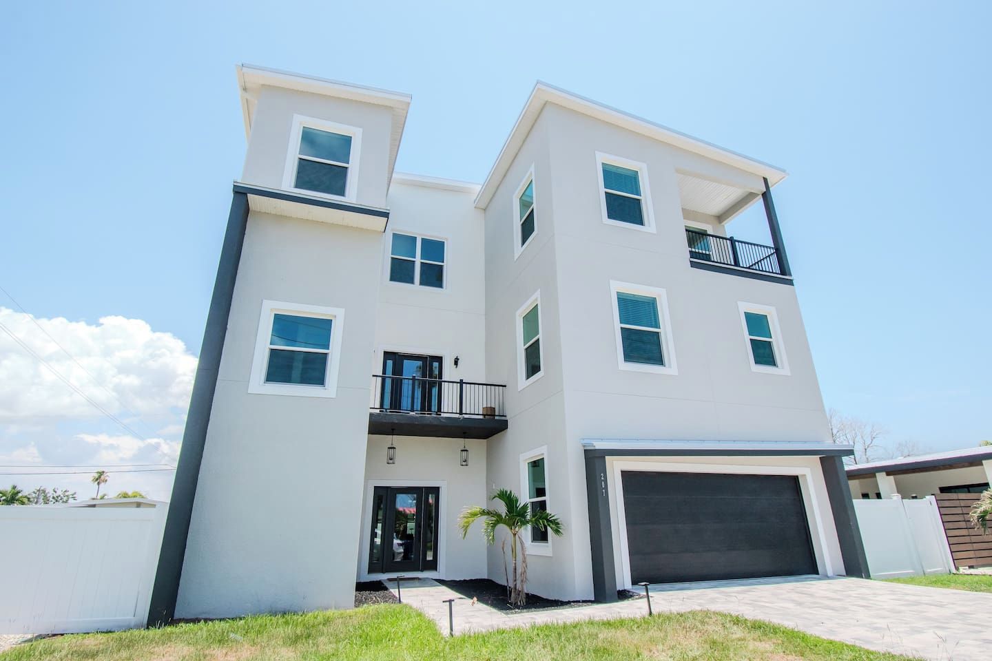 A modern two-story residential building with a garage, a balcony, and a small front yard.