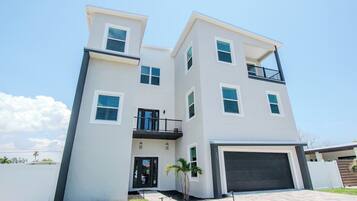 A modern two-story residential building with a garage, a balcony, and a small front yard.