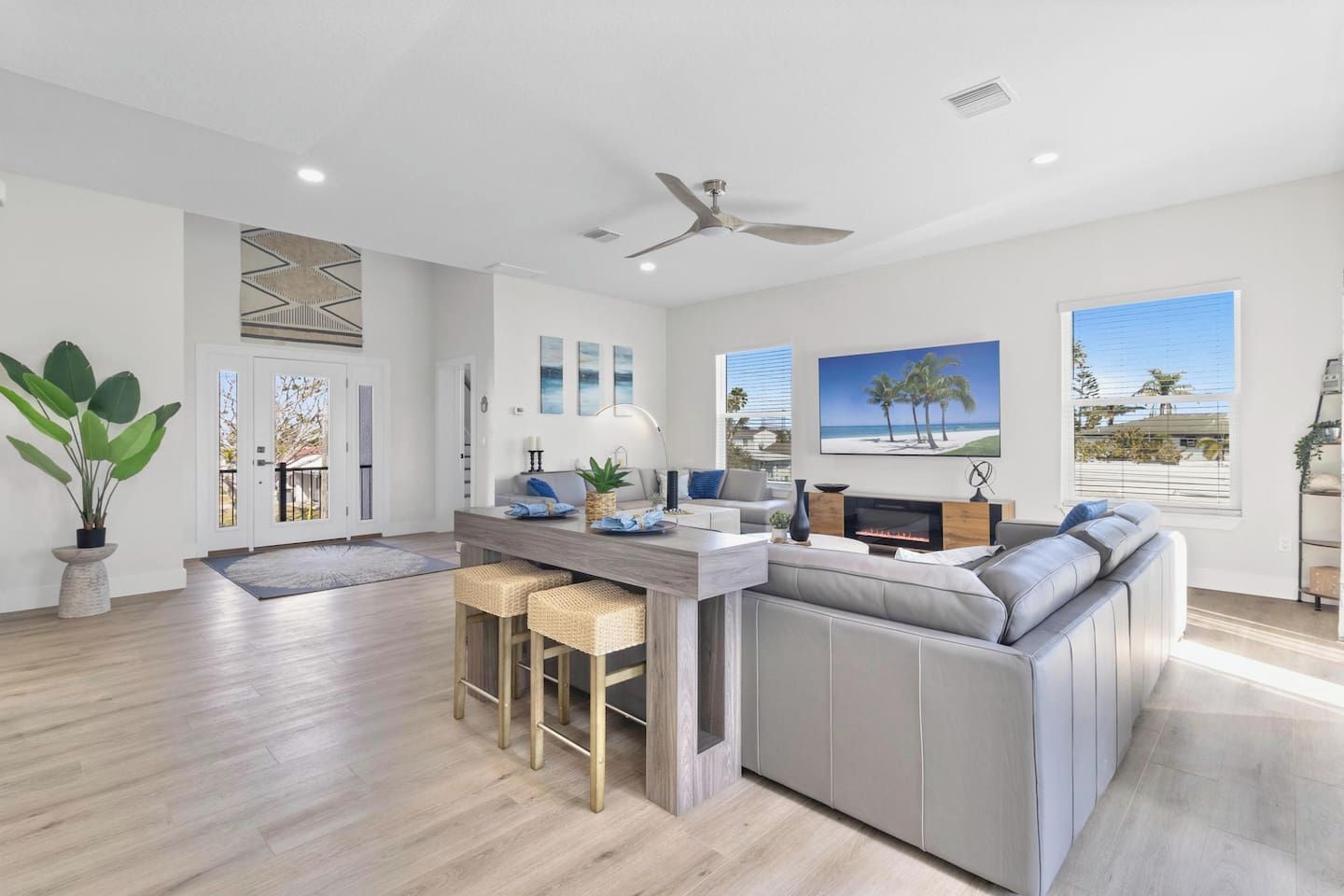 A modern living room with a grey sofa, a dining area with a bar, and a large TV.