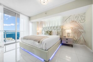 Ein modernes Schlafzimmer mit einem großen Bett, einem Nachttisch, einer Wandmalerei und Blick aufs Meer.