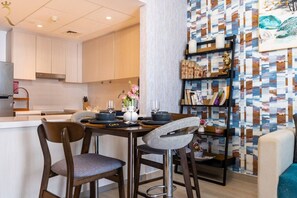 Une cuisine moderne avec un coin repas, comprenant un tabouret de bar, une table dressée pour deux personnes et une bibliothèque contenant des livres et des objets décoratifs.