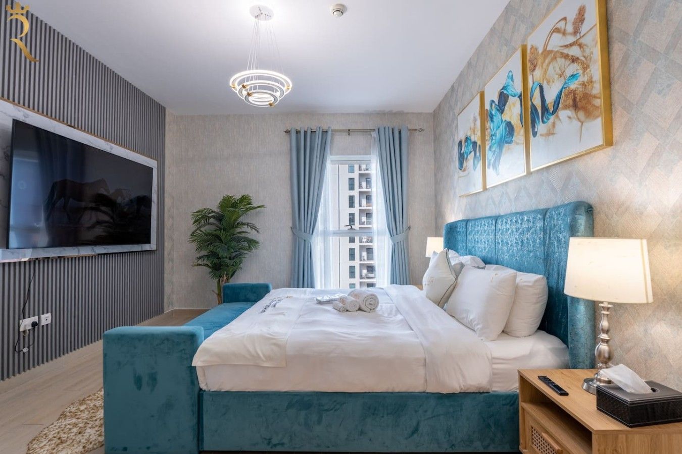 A hotel room with a bed, a TV, a plant, and artwork on the wall.