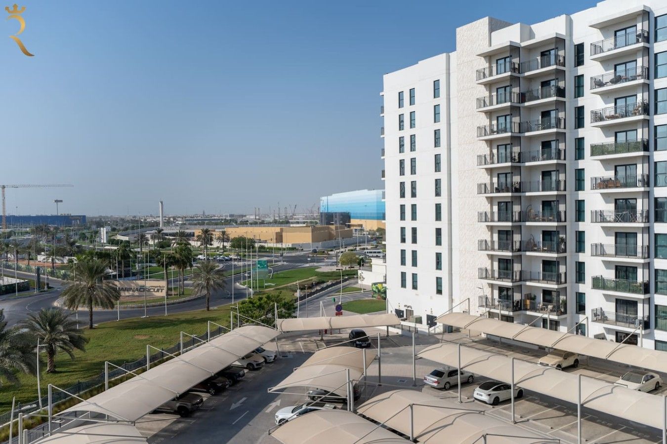 A multi-story residential building with balconies, a parking area, and a view of a coastal area.
