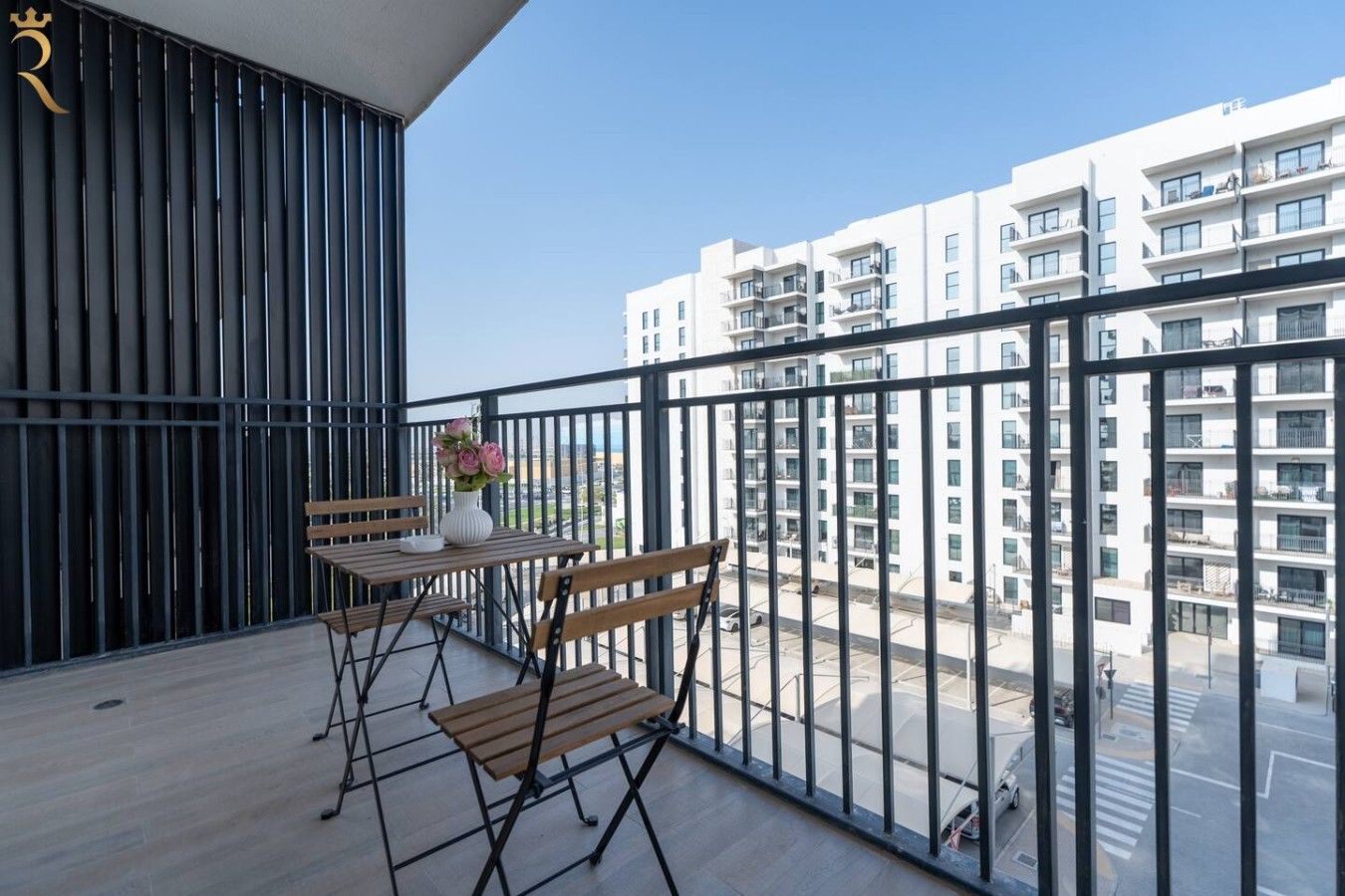 Un balcón con una mesa y sillas, un florero con flores y vistas a un edificio residencial.