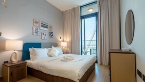 Ett hotellrum med en säng, sängbord, ett skrivbord, en stol och ett stort fönster med gardiner.