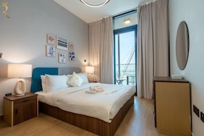 A hotel room with a bed, bedside tables, a desk, a chair, and a large window with curtains. - 1BR Sea View | Private Balcony | Maryah Vista (Abu Dhabi)
