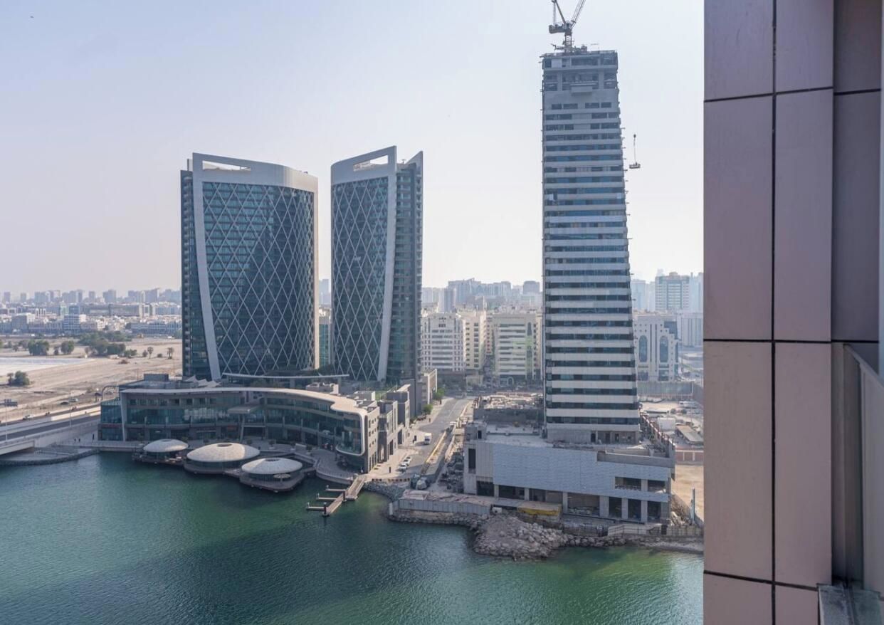Un immeuble de grande hauteur doté d’une façade géométrique originale, situé près d’un front de mer où se trouve un port de plaisance.