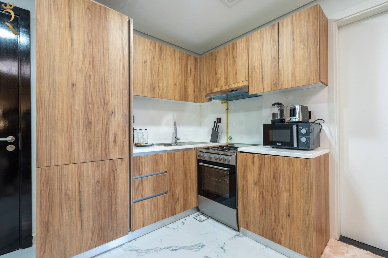 A compact kitchen with wooden cabinets, a stove, an oven, a microwave, and a sink.