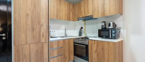 A compact kitchen with wooden cabinets, a stove, an oven, a microwave, and a sink.