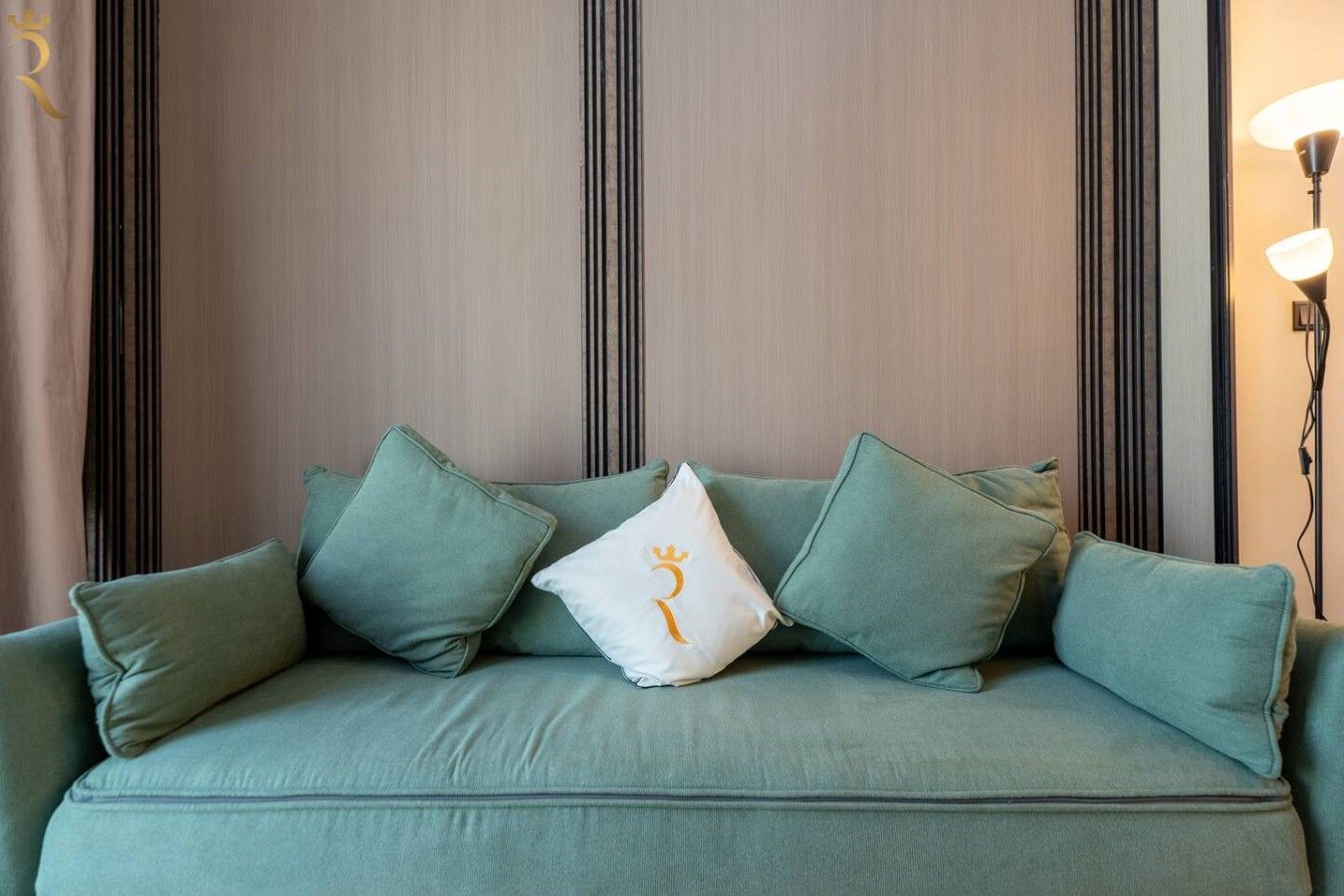 A green sofa with multiple cushions and a white pillow with a symbol.