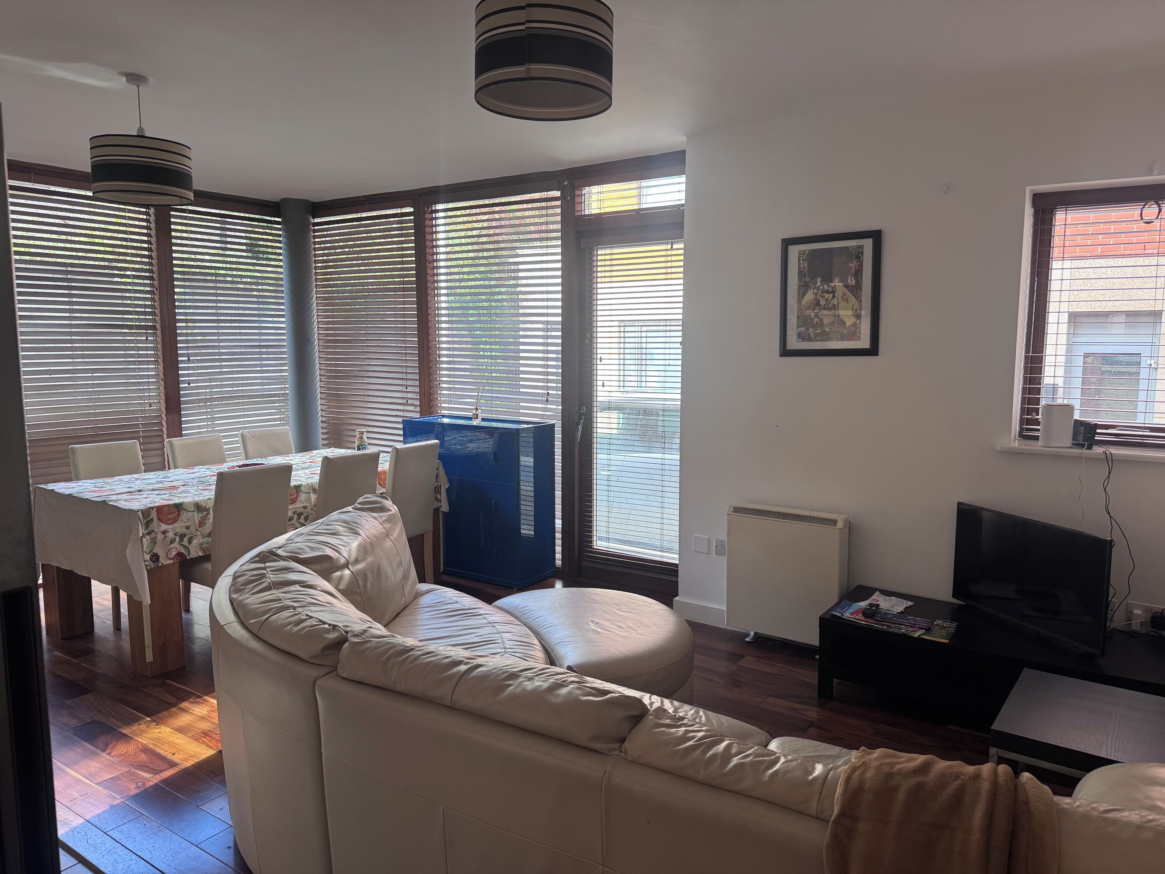 A living room with a sofa, a dining table with chairs, a blue cabinet, a television, and a radiator.