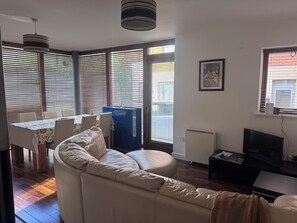 A living room with a sofa, a dining table with chairs, a blue cabinet, a television, and a radiator. - Dublin City Centre Spacious yet Cosy 2B in the Heart of Historic Dublin (Dublin)