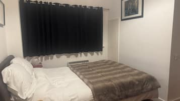 A bedroom with a bed, a bedside table, a heater, a curtain, a door, and a framed picture on the wall.