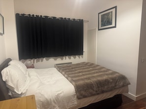 A bedroom with a bed, a bedside table, a heater, a curtain, a door, and a framed picture on the wall. - Spacious Dublin City Centre 2 Apartment w/Gym on site. (Dublin)