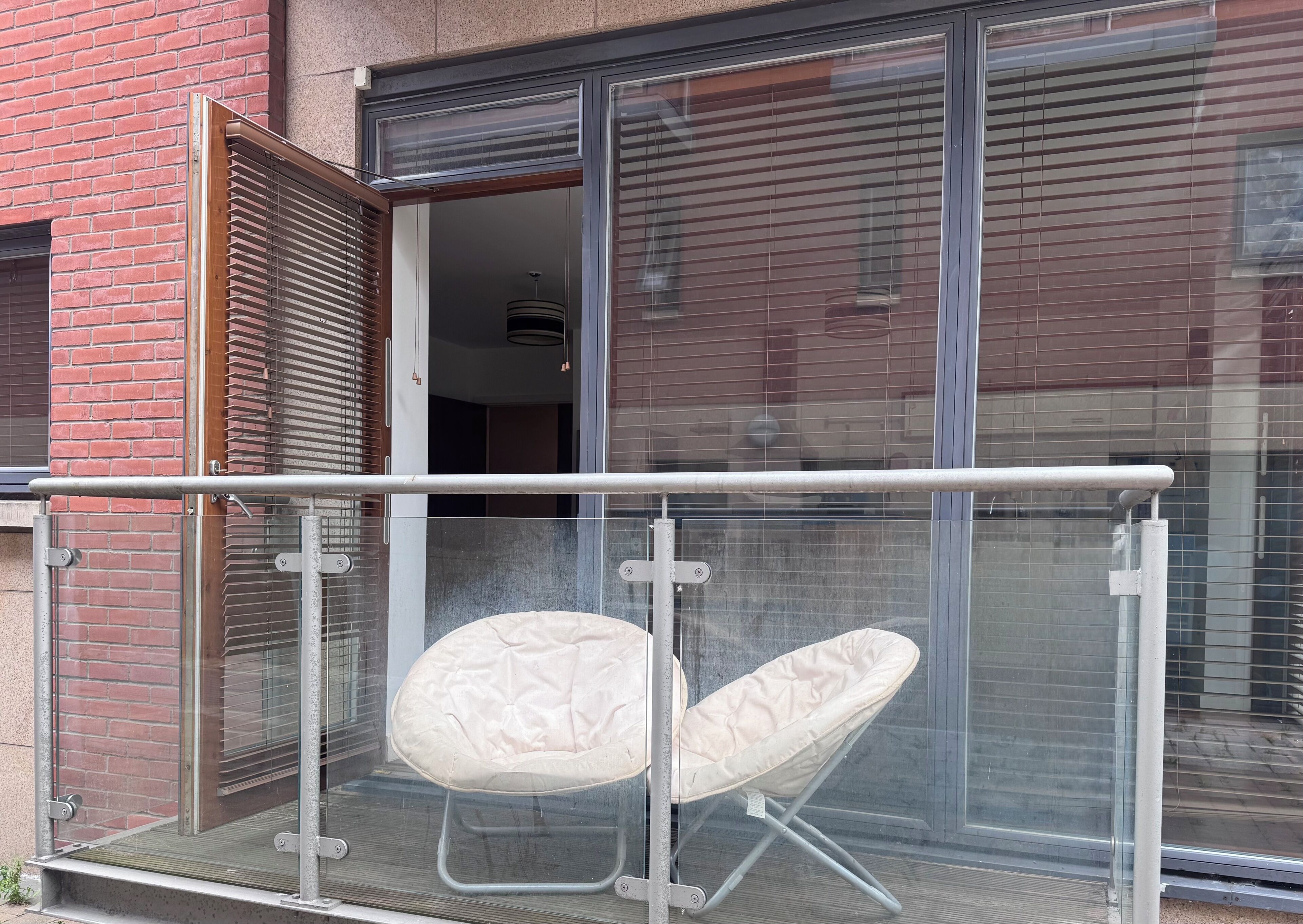A balcony with a glass railing, a cushioned chair, and a sliding glass door leading to an interior space.