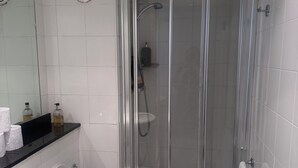 Et moderne badeværelse med en bruseniche med glasvægge, et hvidt toilet og en vask med et spejl over.