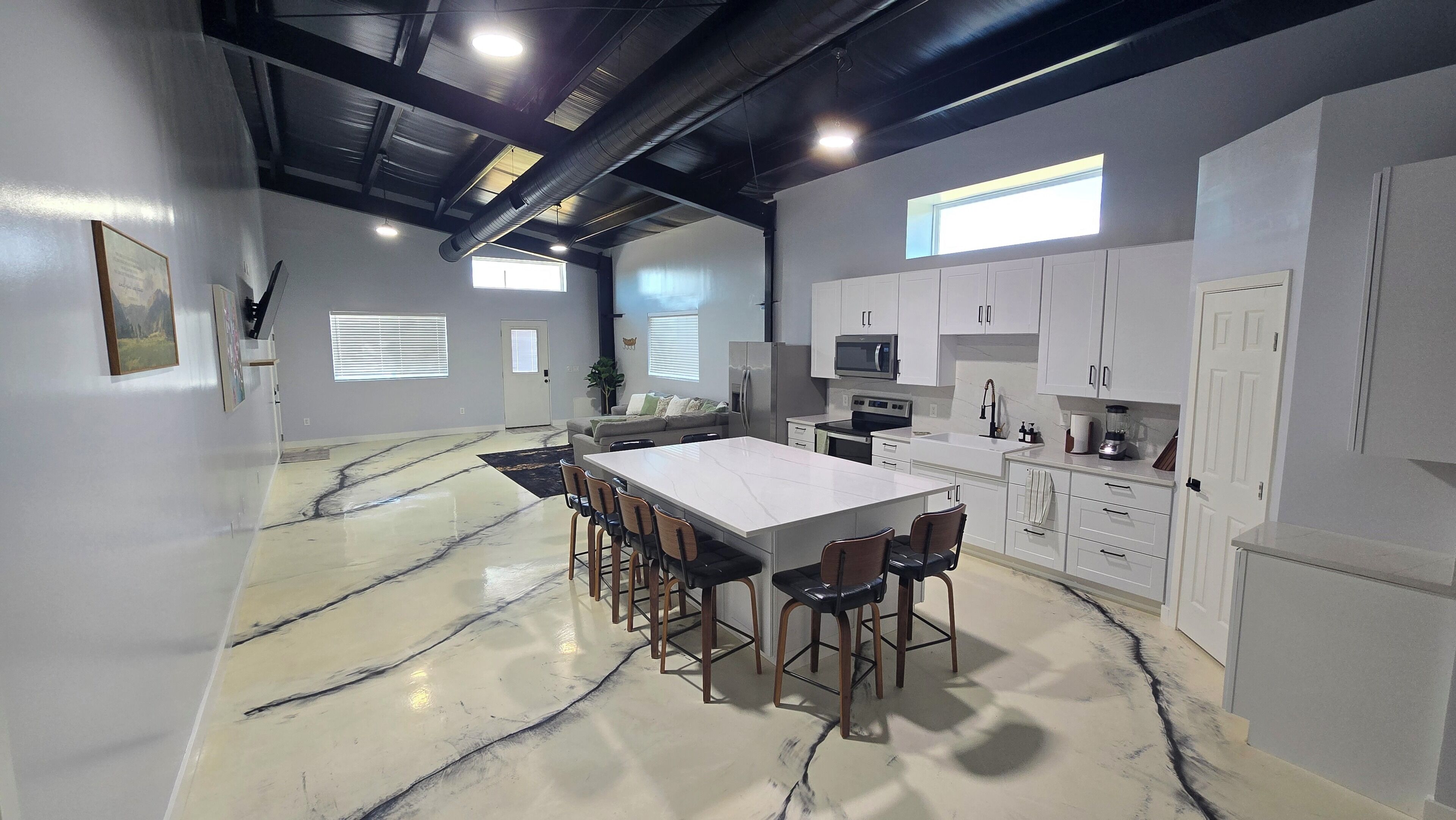 A spacious kitchen with a large island, white cabinetry, and a marble floor.