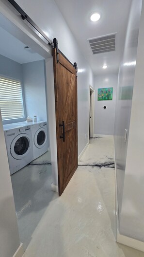 A laundry room with two front-loading washing machines, a wooden sliding door, and a hallway leading to another room. - Spacious Barndominium in Poolville (Poolville)