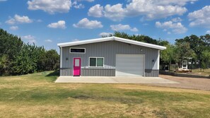 A single-story building with a garage, a pink door, and a window. - Spacious Barndominium in Poolville (Poolville)