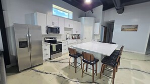 A modern kitchen with white cabinetry, stainless steel appliances, and a large island with bar stools. - Spacious Barndominium in Poolville (Poolville)