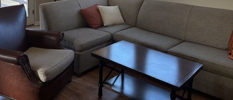 Ett vardagsrum med en hörnsoffa, en fåtölj i läder, ett soffbord och en takfläkt.
