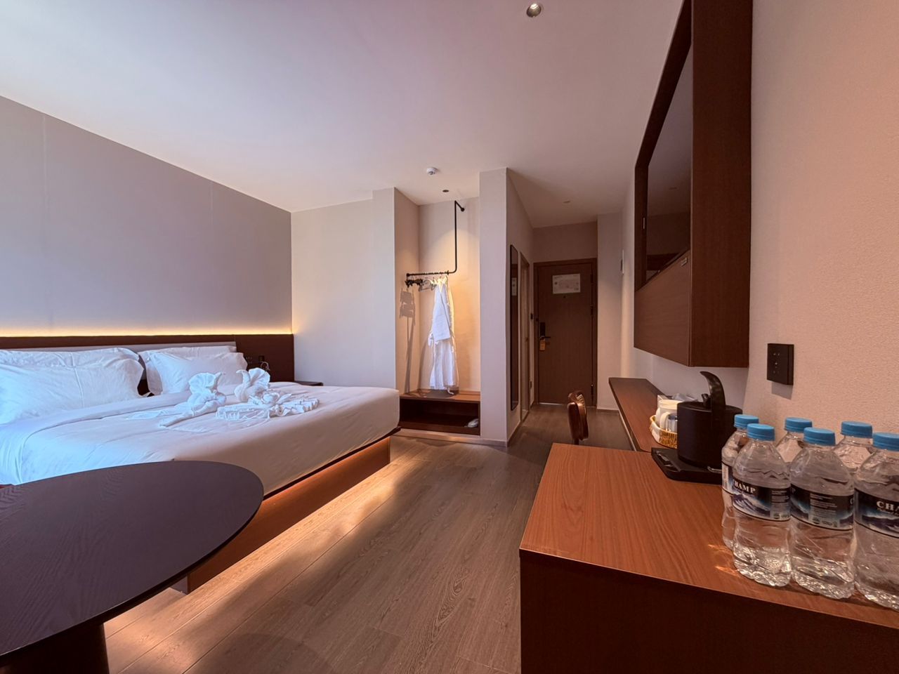 Une chambre d’hôtel avec un lit, un bureau et une chaise. Il y a des bouteilles d’eau sur le bureau.