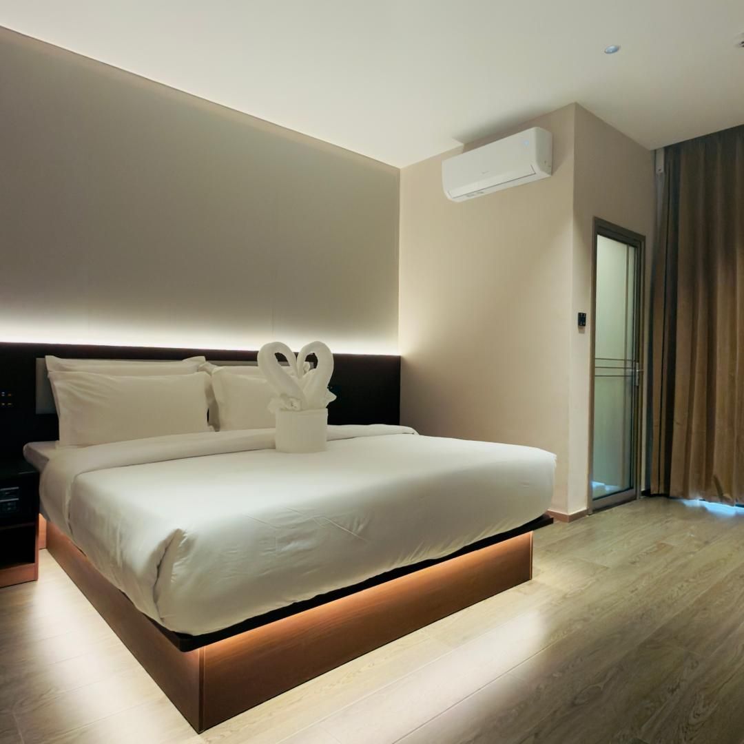 Une chambre d’hôtel moderne avec un grand lit, une table de chevet, un appareil de climatisation et une vue sur l’extérieur grâce à une porte vitrée.