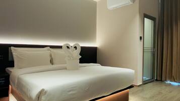 Une chambre d’hôtel moderne avec un grand lit, une table de chevet, un appareil de climatisation et une vue sur l’extérieur grâce à une porte vitrée.