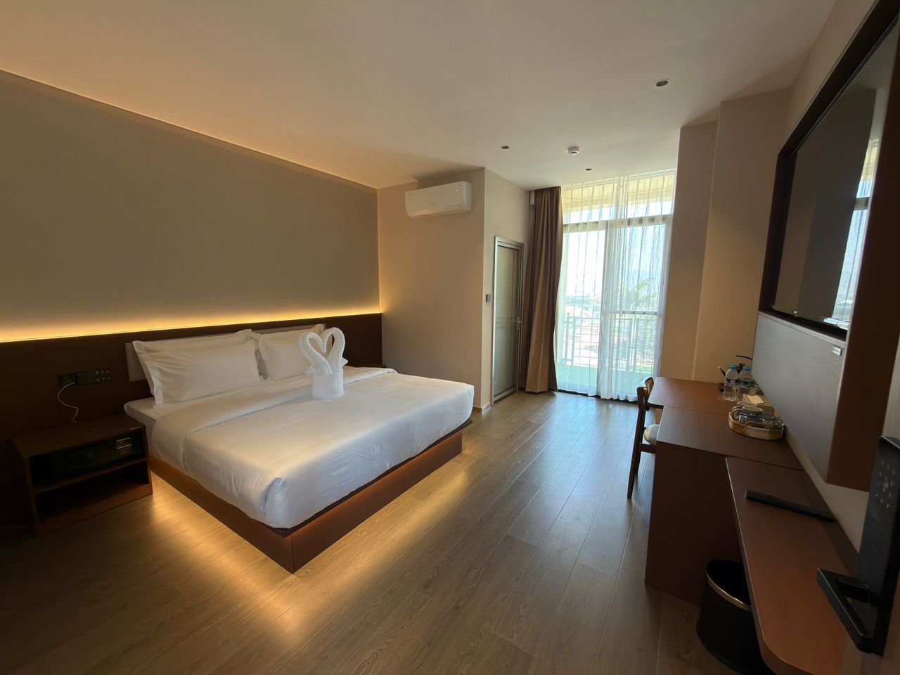 A hotel room with a bed, bedside table, TV, and a view of the outdoors.