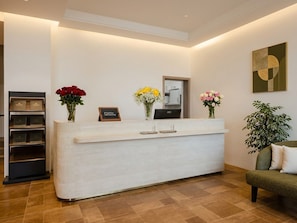 A reception desk with a modern design, a mirror above it, and a potted plant to the right. - Juris Park Hotel (Kigali)