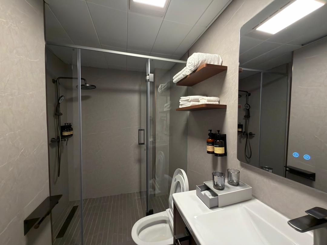 Une salle de bain moderne avec une douche à parois de verre, des toilettes, un lavabo avec un miroir et une étagère avec des serviettes.